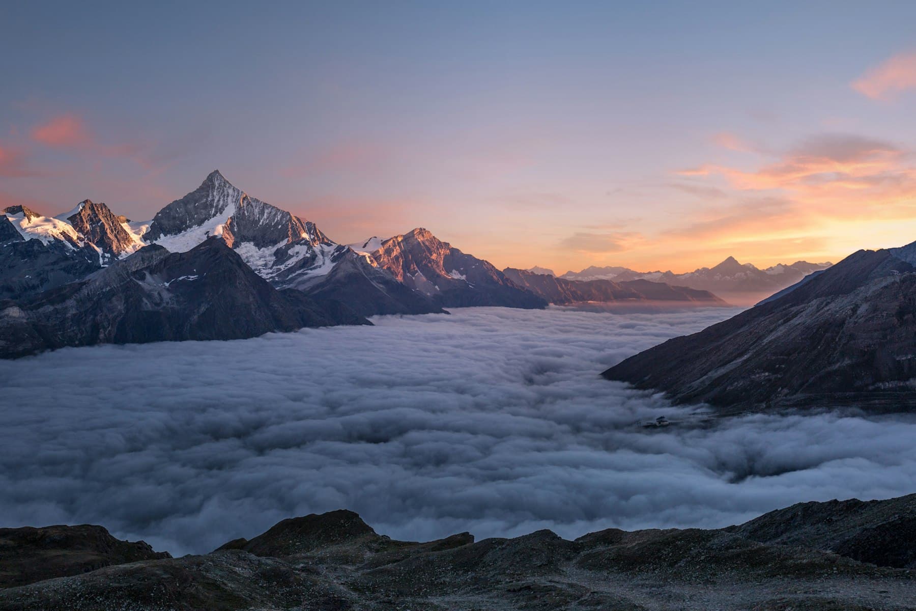 Alpine peaks standing above a sea of clouds at dawn.